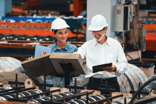 Factory engineer manager with assistant using laptop to conduct inspection of steel industrial machine, exemplifying leadership as machinery engineering inspection supervisor in metalwork manufacture.