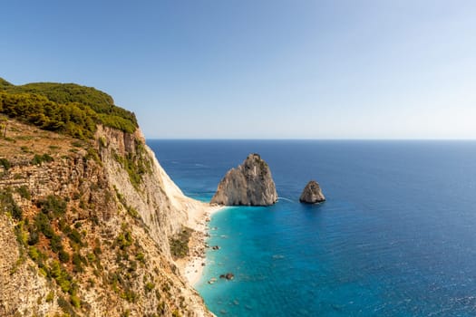 Beautiful view of two rocks in the blue sea with boats sailing in the distance near the beach coastline on a summer sunny day, side view close up.