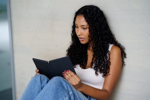A young woman sits comfortably, fully engaged in her ebook, embodying the ideal themes of leisurely activities, the modern art of reading, and the role of technology in todays lifestyle
