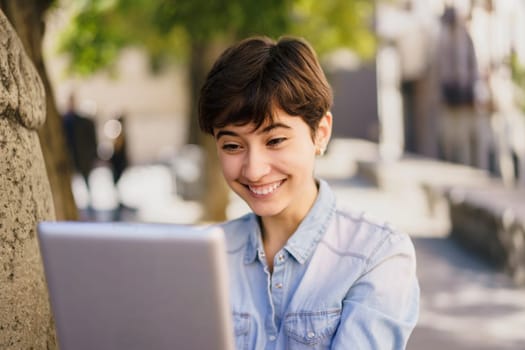 A cheerful young woman is happily engaged in using her laptop outdoors, capturing a wonderful moment of joy and connection with technology in a peaceful and serene natural environment