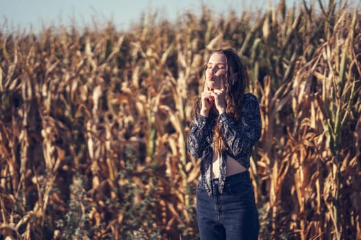 In a vast and vibrant cornfield, a young woman stands amidst towering stalks, savoring a delightful moment of peace and connection with nature, radiating a genuine sense of happiness and tranquility