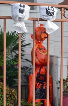 Artificial pumpkin heads from a plastic bag on the fence House in background.