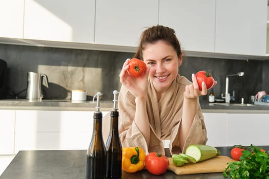 Portrait of beautiful woman cooking in the kitchen, chopping vegetables on board, holding tomatoes, lead healthy lifestyle with preparing fresh salads, vegan meals.