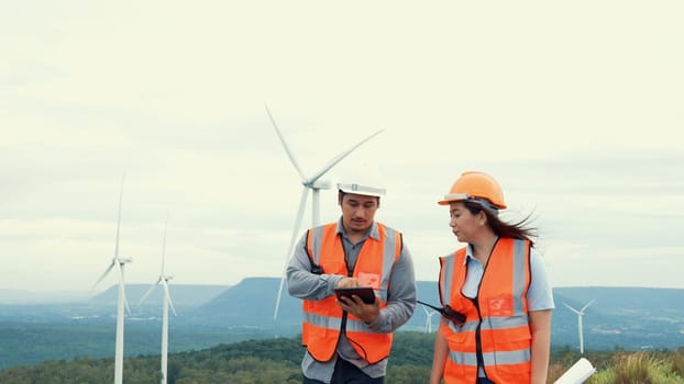 Male and female engineers working on a wind farm atop a hill or mountain in the rural. Progressive ideal for the future production of renewable, sustainable energy.