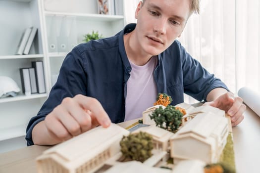 Architect designer studies elegant house model, reviewing structure design for improvement with construction plan on table. Creativity and innovation in architectural design. Iteration