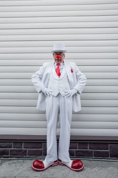 Full-length portrait of a clown in a white classic suit and a vintage tall hat