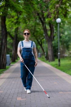 Blind pregnant woman walking in the park with a cane
