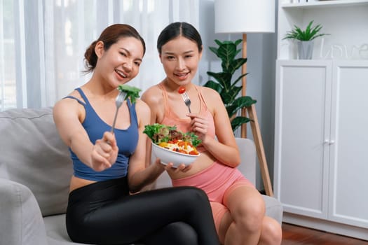 Young sporty Asian women in sportswear holding salad bowl together fill with vibrant of fruit and vegetable. Natural youthful and fit body lifestyle with balance nutrition and home exercise. Vigorous