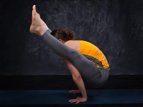 Beautiful sporty fit yogini woman practices yoga asana titibhasana - firefly pose on dark background