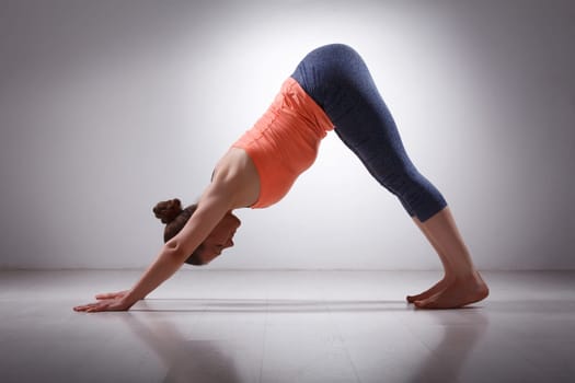 Beautiful sporty fit yogini woman practices yoga asana adhomukha svanasana - downward facing dog pose in studio