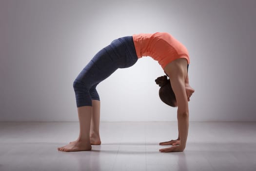 Beautiful sporty fit yogini woman practices yoga asana chakrasana (or urdva dhanurasana) - wheel pose (or upward facing bow) pose in studio