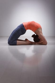 Beautiful sporty fit yogini woman practices yoga asana Kapotasana - pigeon pose intense backbend in studio