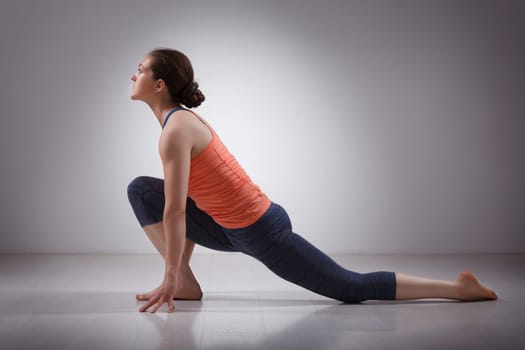 Beautiful sporty fit yogini woman practices yoga asana Anjaneyasana - low crescent lunge pose in surya namaskar in studio