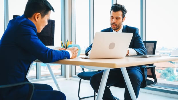 Two business people talk project strategy at office meeting room. Businessman discuss project planning with colleague at modern workplace while having conversation and advice on financial report. Jivy