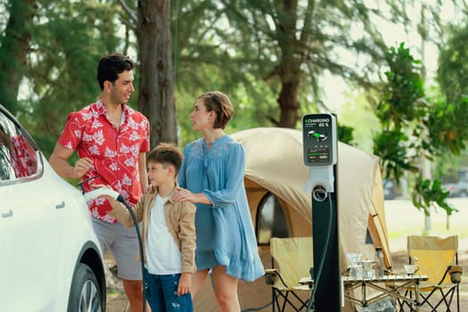 Outdoor adventure and family vacation camping in nature travel by eco friendly car for sustainable future. Lovely family recharge EV car with EV charging station in campsite. Perpetual