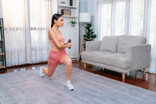 Vigorous energetic woman doing yoga and weight lifting exercise at home. Young athletic asian woman strength and endurance training session as home workout routine.