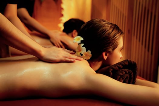 Caucasian couple customer enjoying relaxing anti-stress spa massage and pampering with beauty skin recreation leisure in warm candle lighting ambient salon spa at luxury resort or hotel. Quiescent