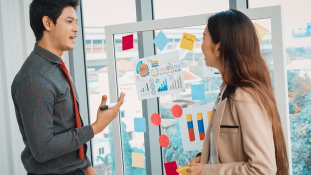 Business people work on project planning board in office and having conversation with coworker friend to analyze project development . They use sticky notes posted on glass to make it organized. Jivy