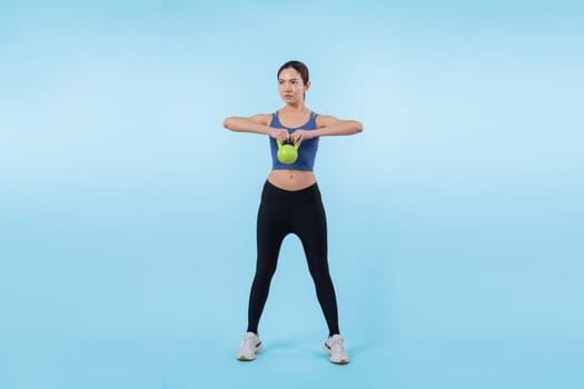 Vigorous energetic woman doing kettlebell weight lifting exercise on isolated background. Young athletic asian woman strength and endurance training session as body workout routine.