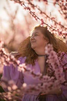 Woman blooming peach orchard. Against the backdrop of a picturesque peach orchard, a woman in a long pink dress and hat enjoys a peaceful walk in the park, surrounded by the beauty of nature