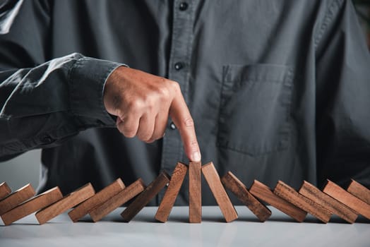 Finger of businessman pointing one wooden to stopping domino effect stopped, Close up hand stopping or preventing falling block in line with risk, Risk protection concept