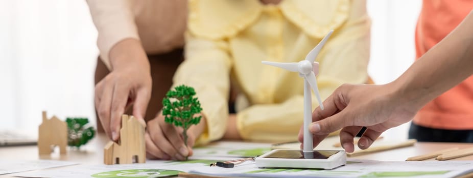 Windmill model represented using renewable energy placed during presenting green business on table with wooden block and environmental document scatter around. Closeup. Delineation.