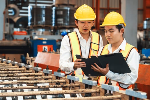 Factory worker operating metal stamping machine while supervised by engineer for optimal quality output of industrial goods on assembly steel forming line in heavy industry factory. Exemplifying