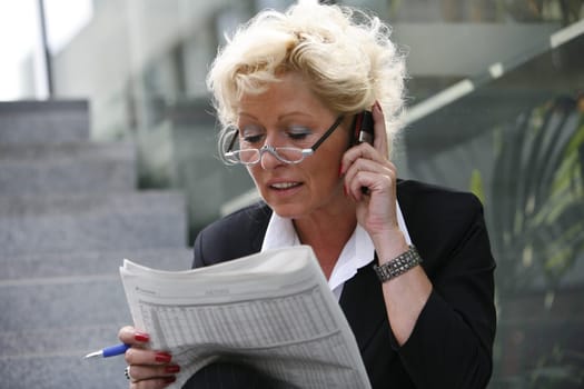 blond woman with newspaper talking on the phone