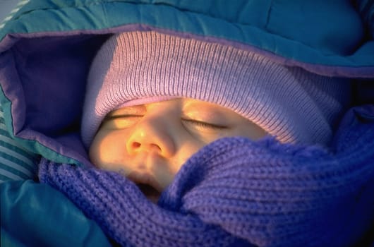 Baby sleeping deeply,wrapped up warm in the evening sun,head portrait,winter
