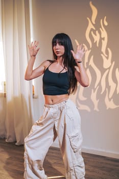 A dancer expresses herself through movement in a bright studio. The warm light casts striking shadows on the wall, enhancing the artistic atmosphere during the performance.