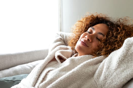 Close up of happy multiracial woman sleeping resting lying on the sofa with arms behind the head at home cozy living room. Copy space. Lifestyle concept.