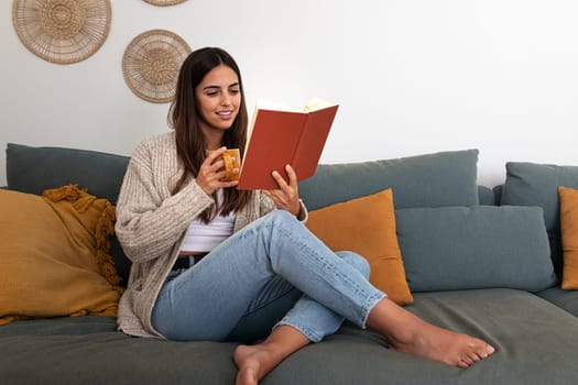 Pensive relaxed caucasian woman reading a book at home, drinking coffee sitting on the couch. Copy space. Lifestyle concept.