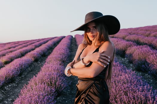 Close up portrait of young beautiful woman in a white dress and a hat is walking in the lavender field and smelling lavender bouquet.