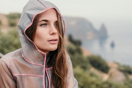 Woman rain park. Happy woman portrait wearing a raincoat with transparent umbrella outdoors on rainy day in park near sea. Girl on the nature on rainy overcast day