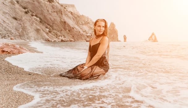 Woman travel sea. Young Happy woman in a long red dress posing on a beach near the sea on background of volcanic rocks, like in Iceland, sharing travel adventure journey