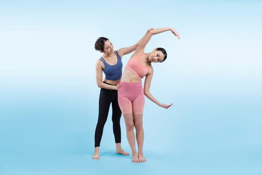 Asian woman in sportswear doing yoga exercise in standing pose with her trainer or yoga buddy. Healthy body care and meditation yoga lifestyle in full shot on isolated background. Vigorous