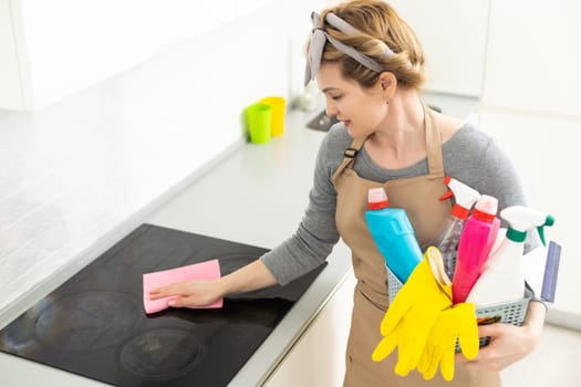 Young woman doing house chores. Woman holding cleaning tools. Woman wearing rubber protective yellow gloves, holding rag and spray bottle detergent. It's never too late to spring clean.