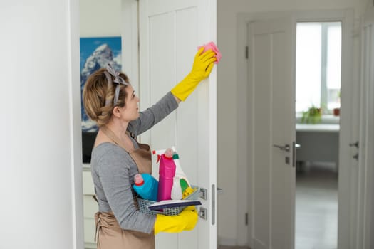 Young woman doing house chores. Woman holding cleaning tools. Woman wearing rubber protective yellow gloves, holding rag and spray bottle detergent. It's never too late to spring clean.