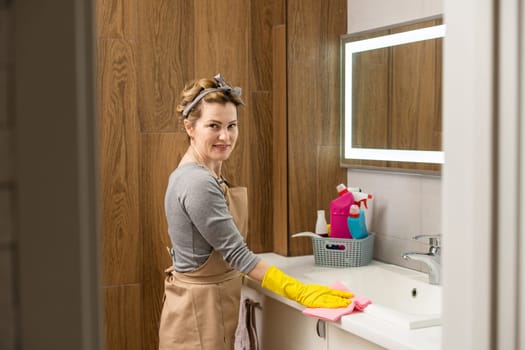 Young woman doing house chores. Woman holding cleaning tools. Woman wearing rubber protective yellow gloves, holding rag and spray bottle detergent. It's never too late to spring clean.