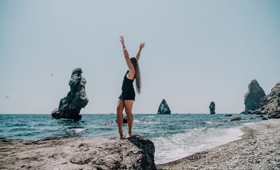 Woman travel sea. Young Happy woman in a long red dress posing on a beach near the sea on background of volcanic rocks, like in Iceland, sharing travel adventure journey