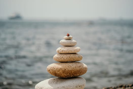 Pyramid stones on the seashore with warm sunset on the sea background. Happy holidays. Pebble beach, calm sea, travel destination. Concept of happy vacation on the sea, meditation, spa, calmness.