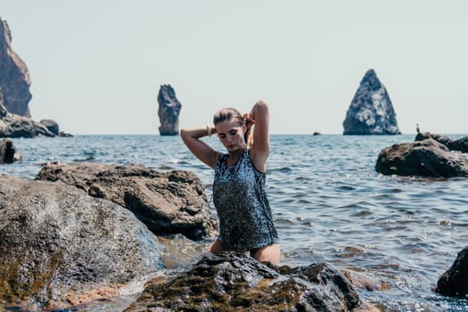 Woman travel sea. Young Happy woman in a long red dress posing on a beach near the sea on background of volcanic rocks, like in Iceland, sharing travel adventure journey