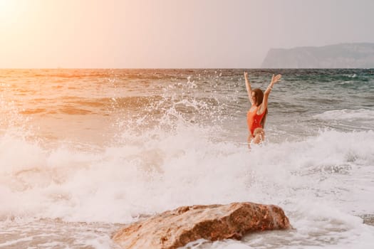 Woman travel sea. Young Happy woman in a long red dress posing on a beach near the sea on background of volcanic rocks, like in Iceland, sharing travel adventure journey