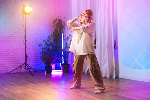 A dancer expresses herself through movement in a vibrant studio. Colorful lights create an energetic atmosphere, while potted plants add a natural touch to the artistic space.