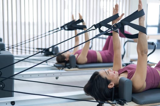 Two young asian women doing pilates exercises on a reformer