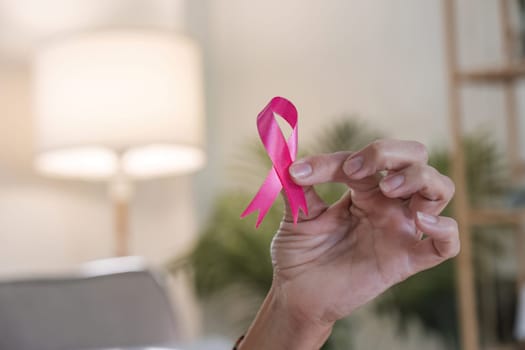 Close-up woman hand holding pink ribbon symbol. Breast cancer awareness and october pink day, world cancer day, national cancer survivor day. healthcare concept.