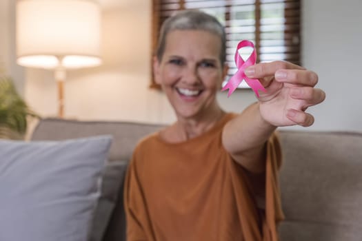 Portrait of confident smiling elderly senior woman with pink ribbon at her home. Health care, support, prevention. Breast cancer awareness month concept.