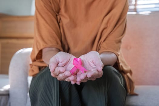 Close-up woman hand holding pink ribbon symbol. Breast cancer awareness and october pink day, world cancer day, national cancer survivor day. healthcare concept.