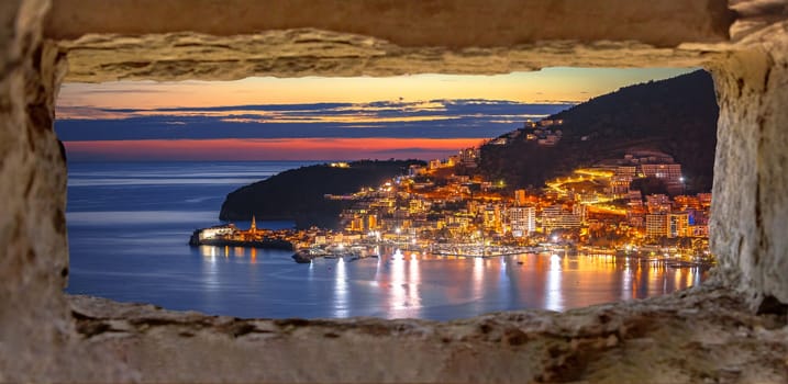 Town of Budva coastline architecture colorful evening view through stone window, archipelago of Montenegro