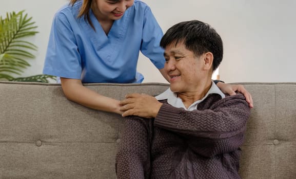 nurse supports man during recovery A caregiver holds the hand of a senior patient who is resting in the living room